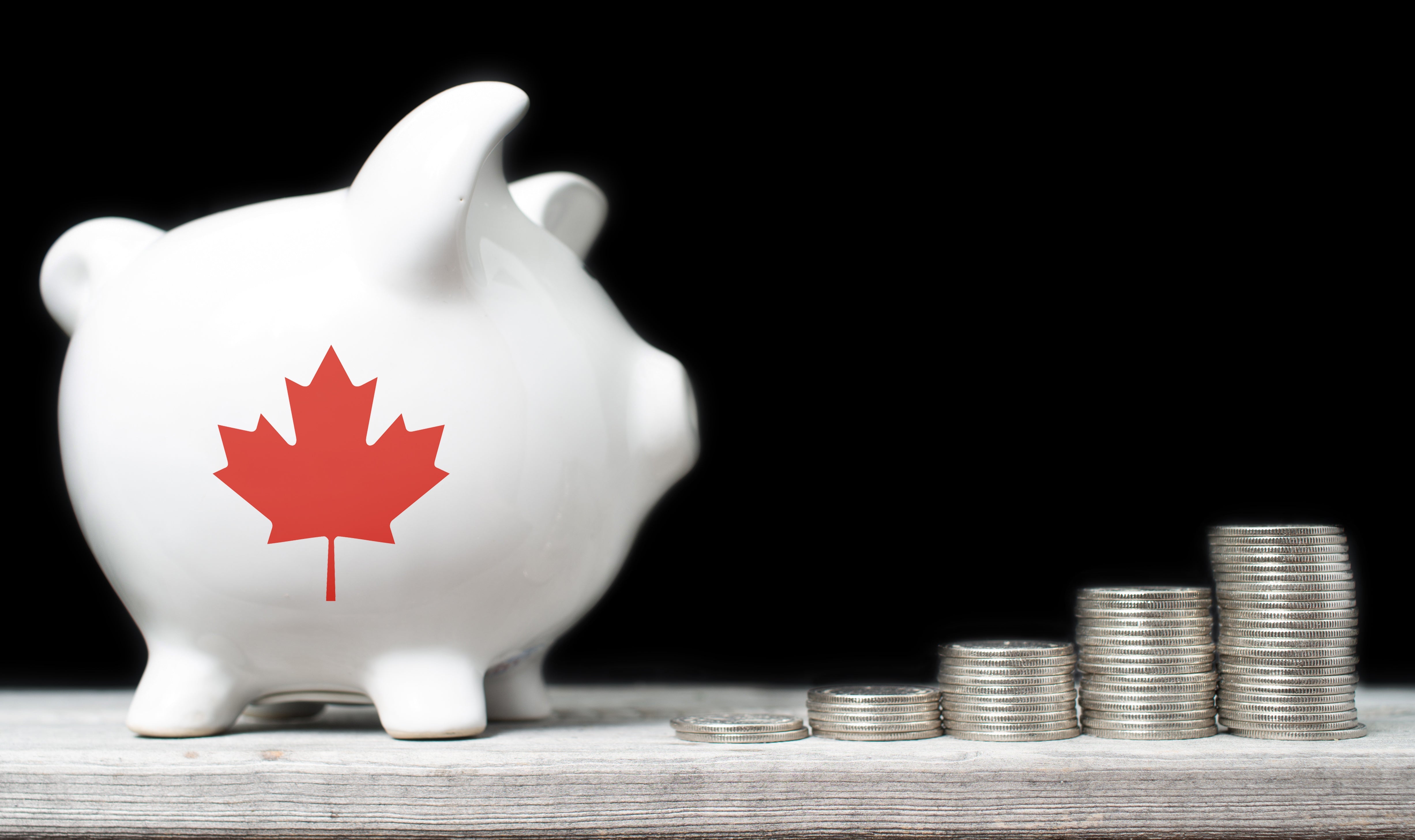 The image features a piggy bank adorned with a Canadian maple leaf, alongside stacks of Canadian coins, symbolizing saving or investing in Canada.