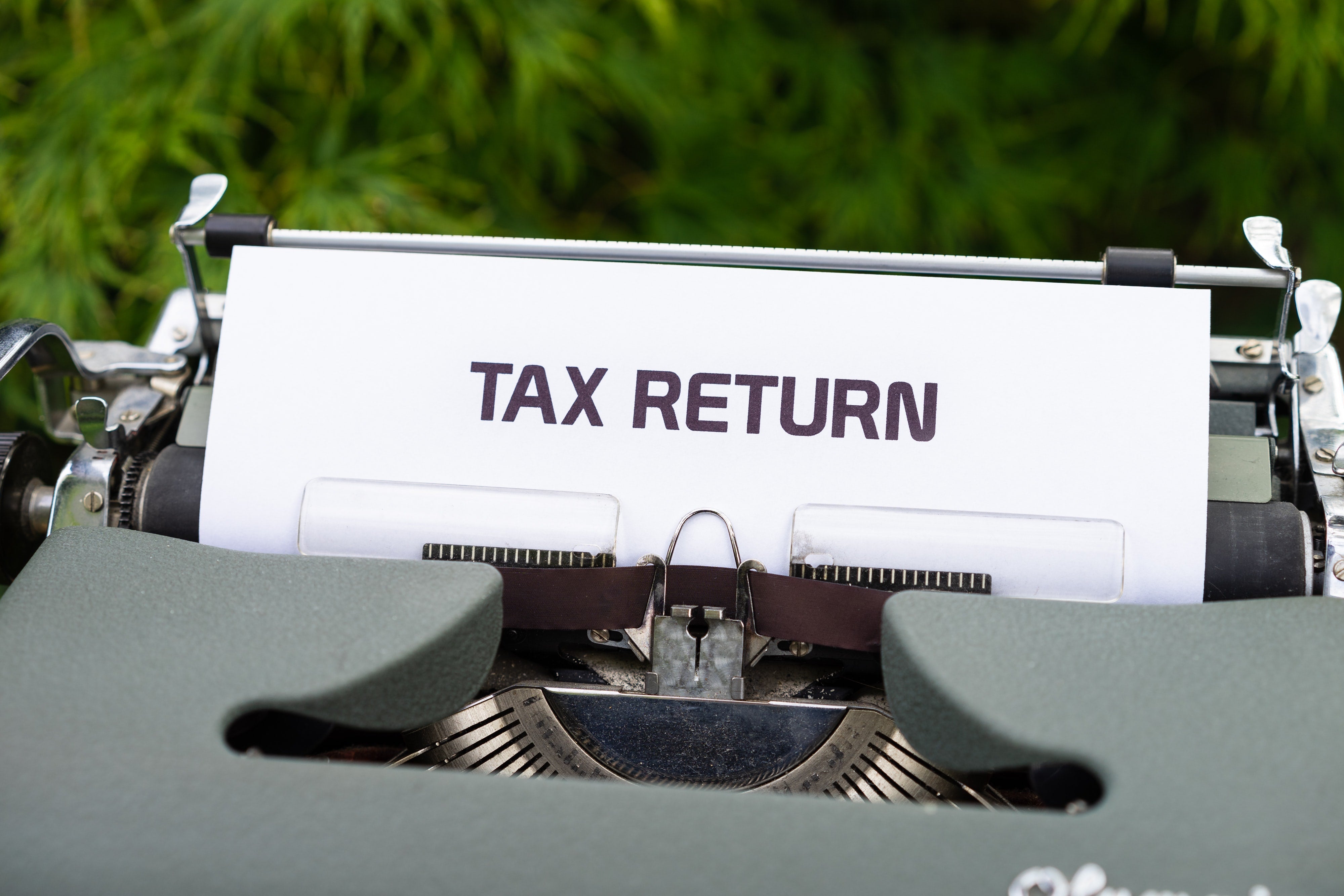A close-up of a vintage typewriter with a sheet of paper inserted, displaying the words 'TAX RETURN' typed in bold, dark letters.