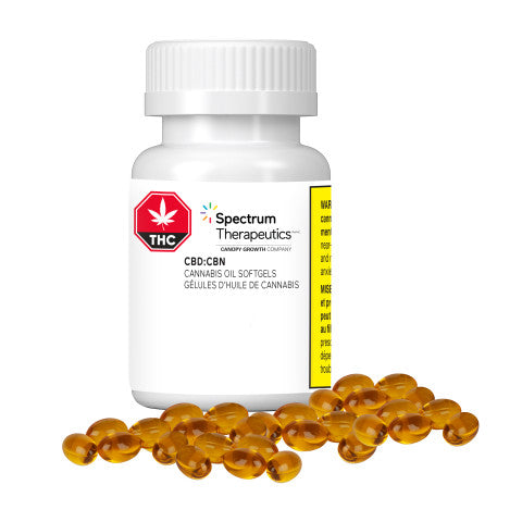A bottle of Spectrum Therapeutics brand softgels, with a label indicating CBD:CBN 2:1 ratio, and a concentration of 20mg CBD and 10mg CBN per softgel. The bottle is accompanied by several orange capsules spilling out in front.