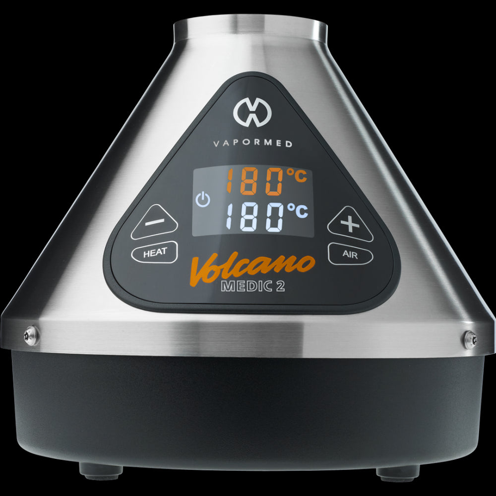 The image shows the Volcano Medic 2 hot air generator, which is a triangular-shaped device with a digital display, touch buttons, and ports for connecting accessories such as balloons and tubes.