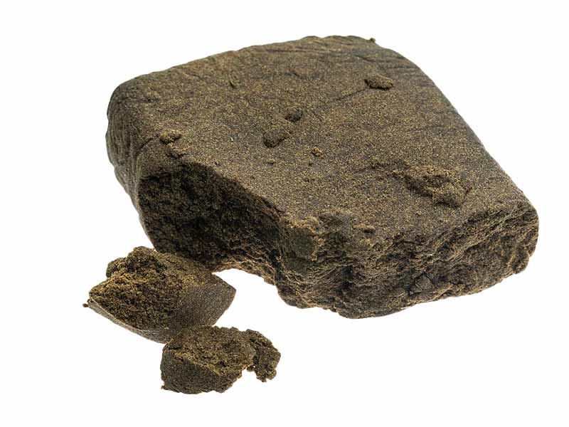A picture of a dark brown, solid block of Moroccan 00 Hash Concentrate with some smaller pieces in front of it.