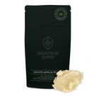 A black Smoke Ops White Apple Rind edible product pouch shown on a white background with a small pile of pale yellowish edible wax melt in front. The pouch has a circular seal at the top right and visible Smoke Ops branding.