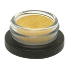 Small glass container with gold powder on a black base against a white background