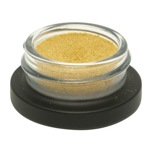 Small glass container with gold powder on a black base against a white background
