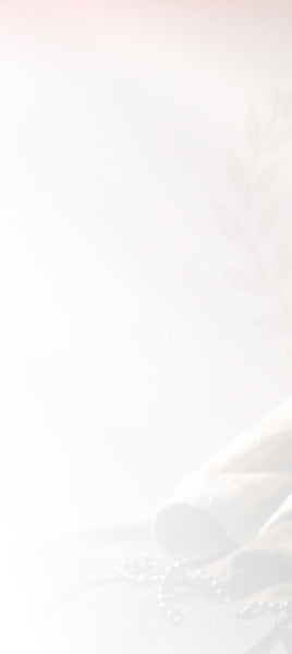 A very light, soft-focus background with faint decorative elements, including a rolled white fabric or towel and pearl-like beads in the lower right corner.