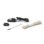 A collection of accessories laid out on a white background, including a black USB charging cable with a magnetic charging dock, a small black rubber or silicone piece, a bundle of beige cotton wick-like strings with red specks, and a small metal cleaning brush.