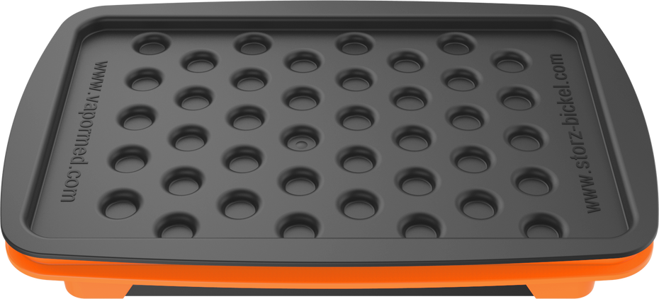 A set of accessories for filling dosing capsules, including a filling device, spatula, plunger, grinder, magazine with sealed capsules, and a scale. The grinder and magazine have orange accents.